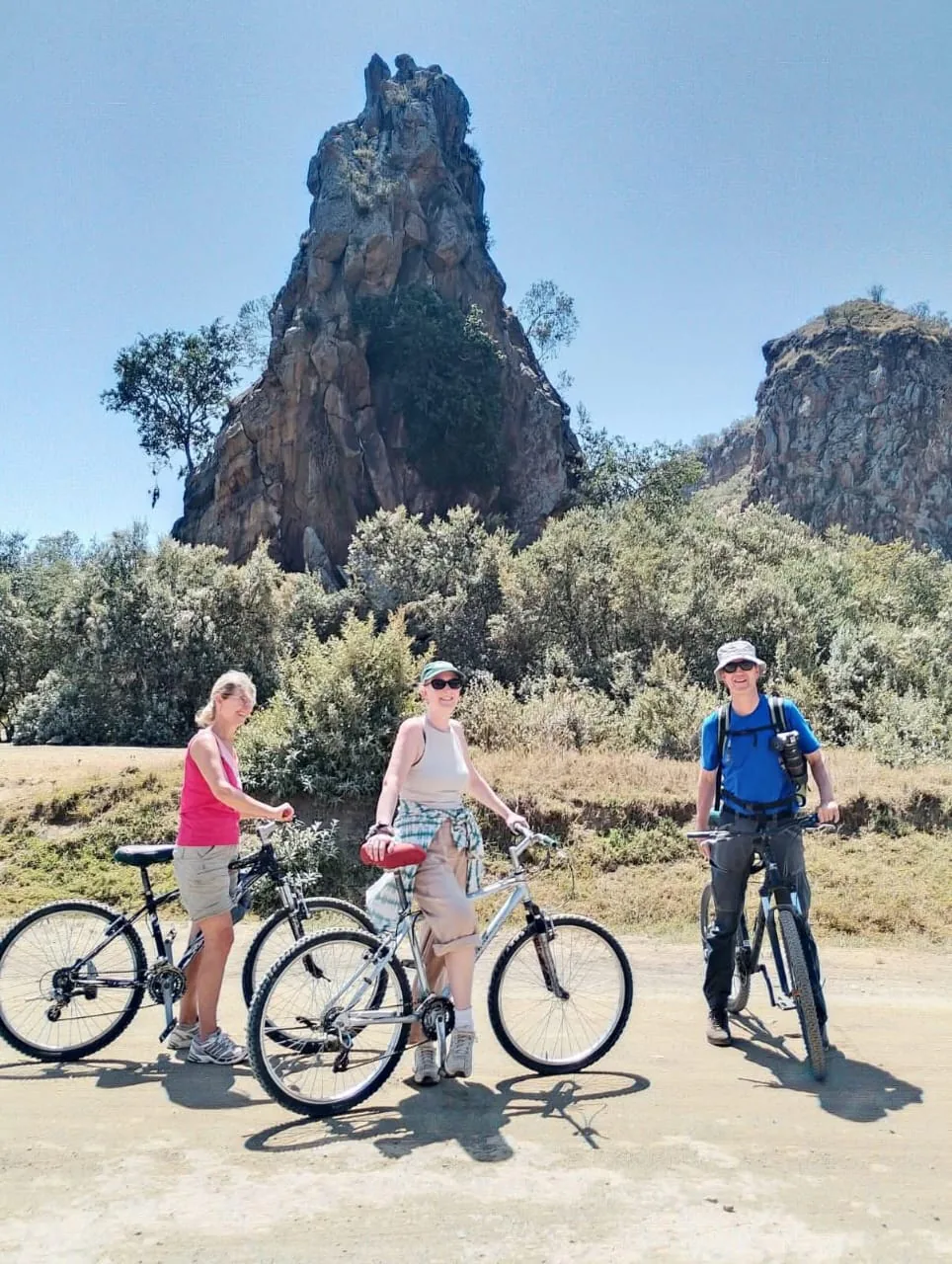 Three travelers with bicycles beneath a tall rock formation